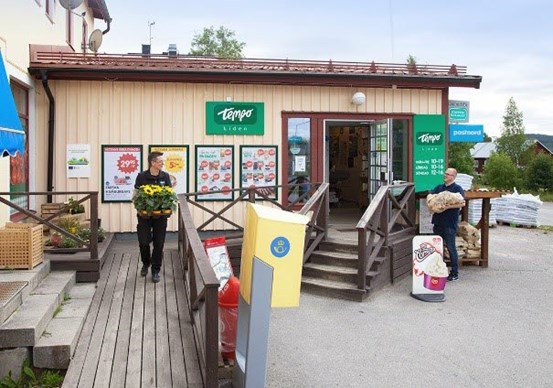 Utsidan av en matvarubutik. Två ur personalen bär pallar med blommor.