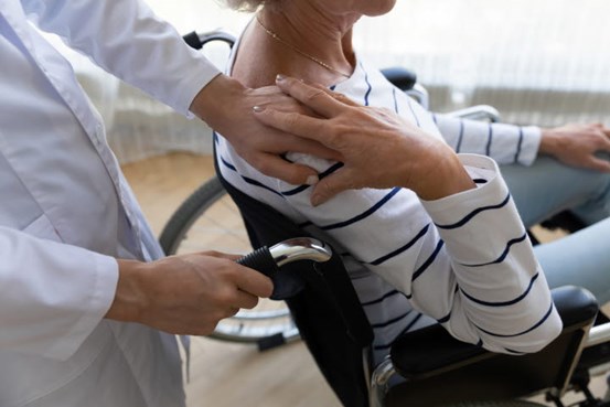 En vårdgivare håller en hand på ena axeln på en person i rullstol