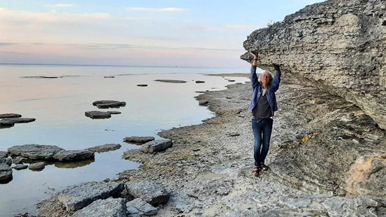 Längs öländsk stenstrand står Janne Björkman med upplyfta armar som om han håller upp ett klippblock. 