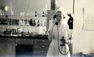En svartvit bild på en kvinna i gammeldags sjuksköterskeklänning. Kvinnan pratar i telefon.