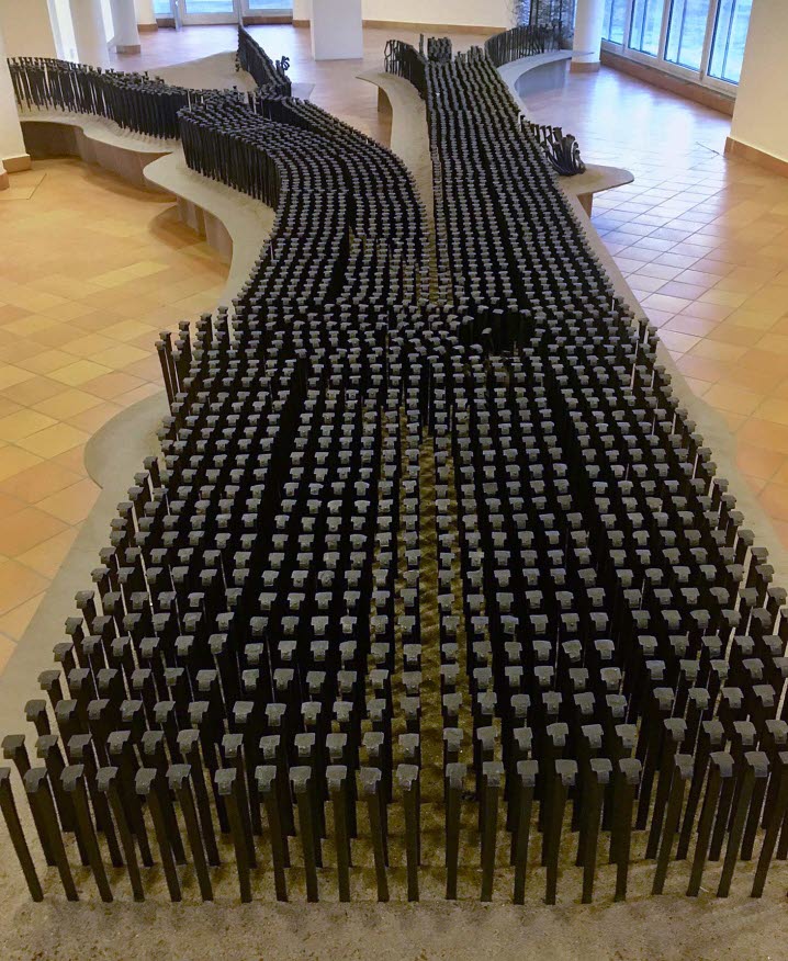 Installationsvy från Kramfors konsthall där flera rälsspikar fyller utställningsgolvet och bildar ett järnvägsspår, som längre fram delar upp sig i två möjliga riktningar. 
