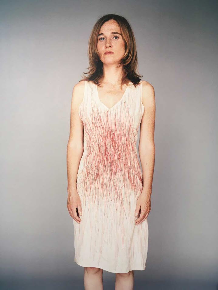 Foto av en person med vit klänning där en röd penna lämnat tydliga spår, vilka påminner om blodiga sår och snitt.