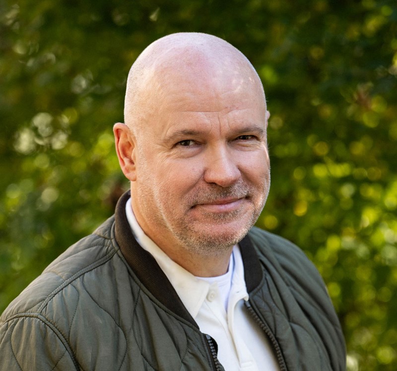 Författaren Jan Melander i grön jacka utomhus. Suddig bakgrund.