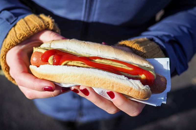 Ett par händer med rött nagellack håller i en varmkorv med ketchup och senap.