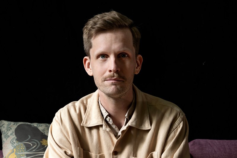 Foto, porträtt av Robin Olovssson. Mörk bakgrund. Fotograf: Sofia Runarsdotter.